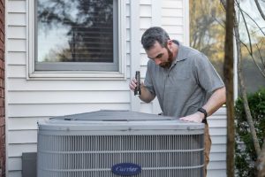 HVAC technician inspecting outdoor AC unit for spring maintenance in Ottawa